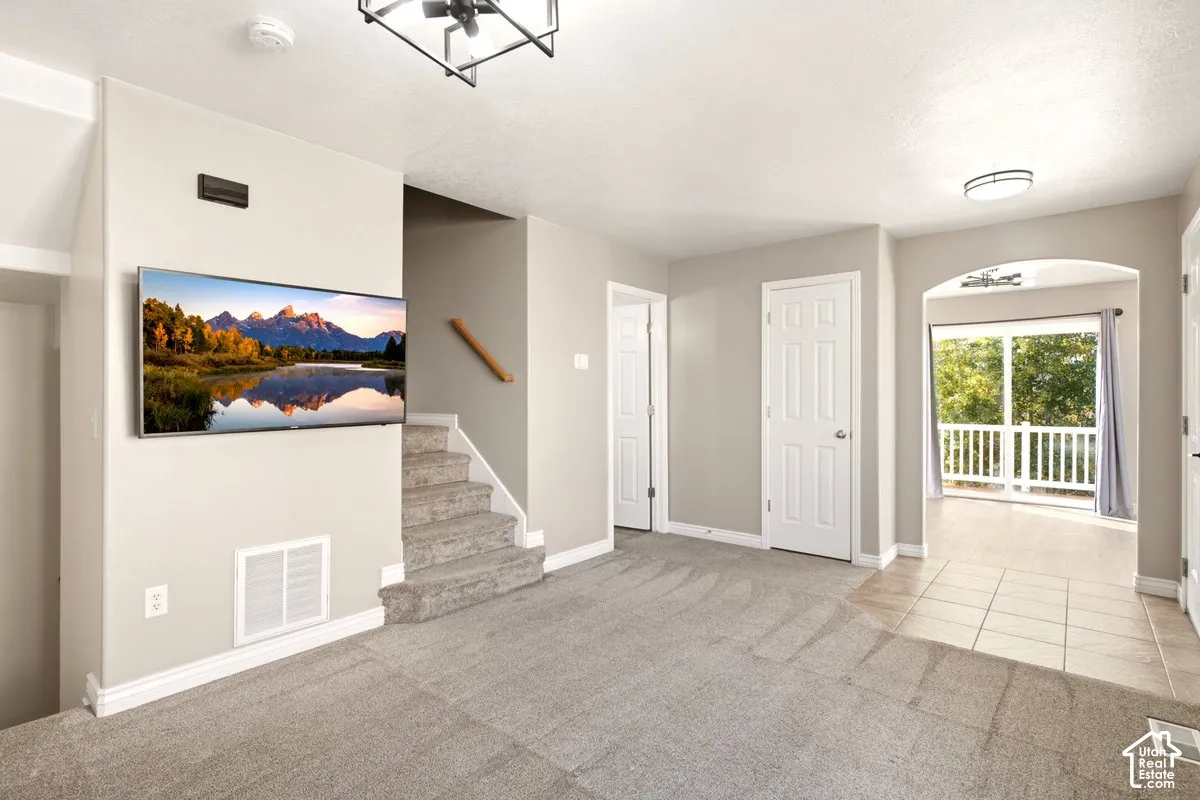 Interior space featuring neutral wall tones, carpeted flooring, a geometric matte black light fixture, and an arched entryway leading to a deck
