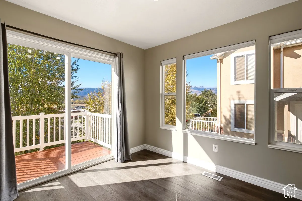 Room featuring wood-finish flooring, large windows, and a sliding glass door providing access to a deck with mountain scenery