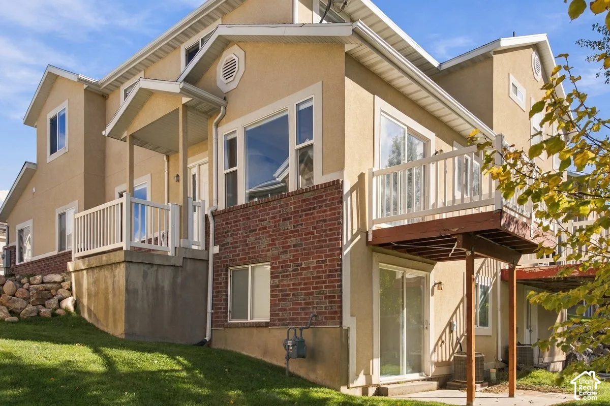 Multi-level exterior featuring stucco and brick siding, elevated wood deck with white railings, concrete patio, and stone retaining wall