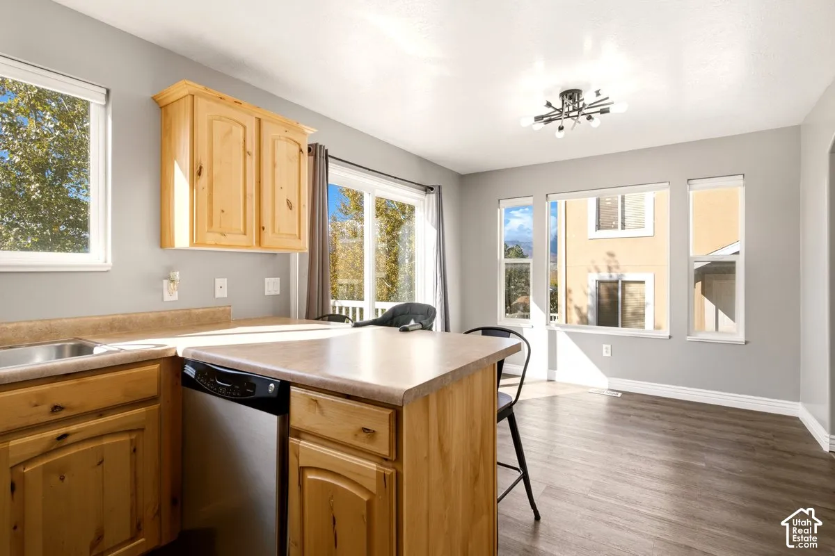 Kitchen featuring wood-finish cabinetry, solid surface countertops, stainless steel dishwasher, wood-finish flooring, and multi-arm geometric light fixture