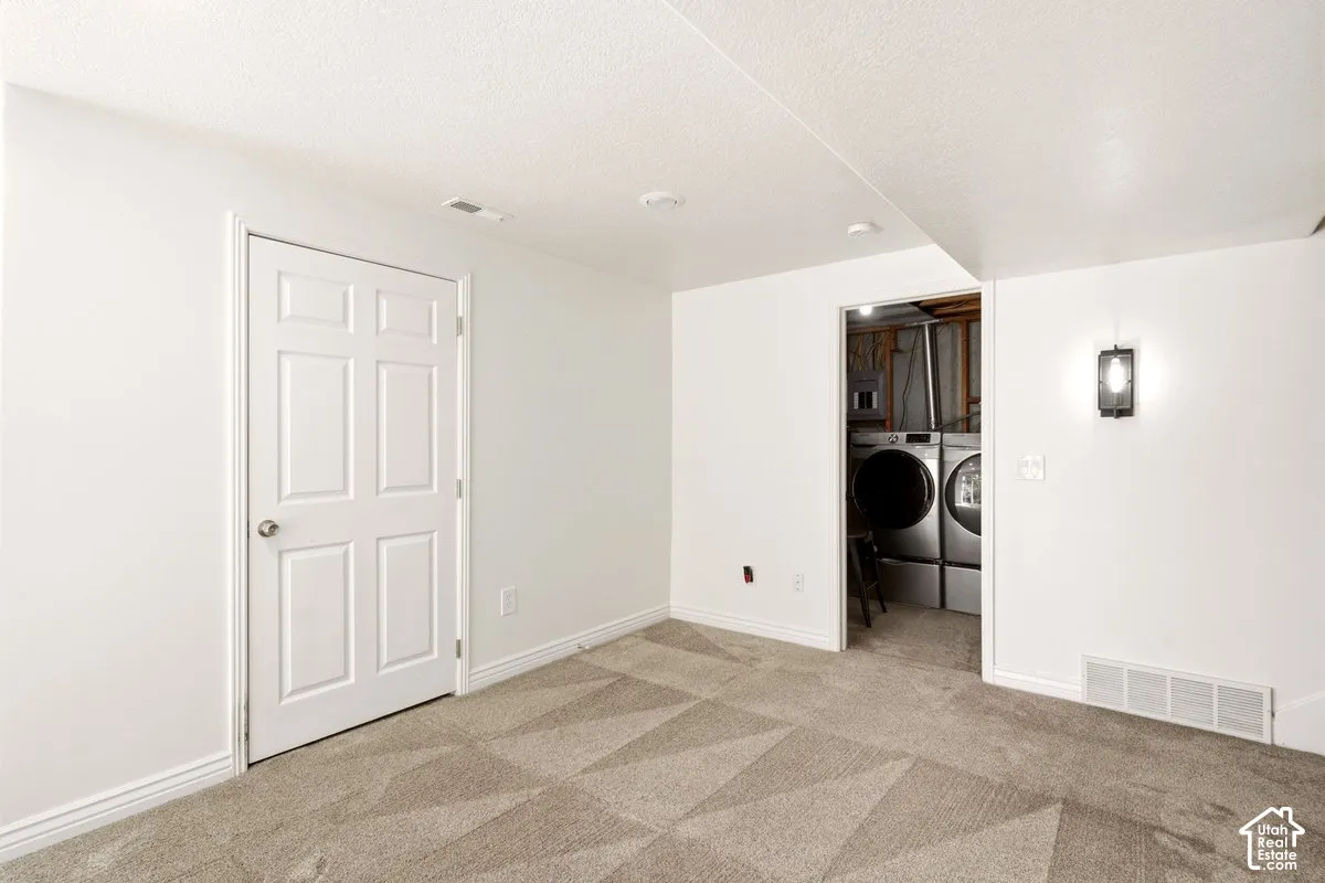 Neutral-toned patterned carpeting, six-panel interior door, wall-mounted light fixture, and recessed laundry area