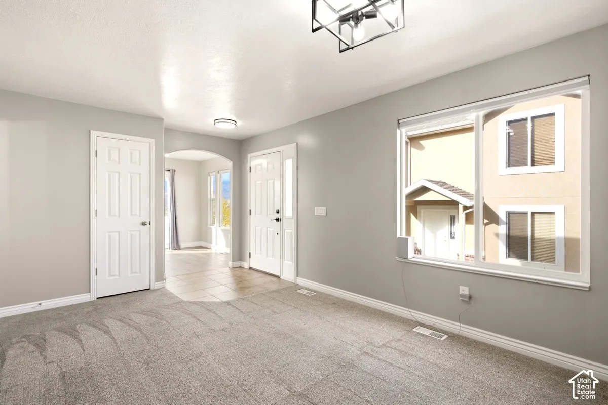 Neutral-toned interior featuring wall-to-wall carpeting, an oversized window, a geometric metal chandelier, and a decorative arched entryway