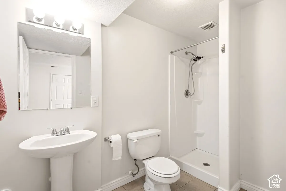 Bathroom featuring a pedestal sink, wall-mounted mirror with integrated lighting, two-piece toilet, and a tiled shower stall with a handheld shower fixture