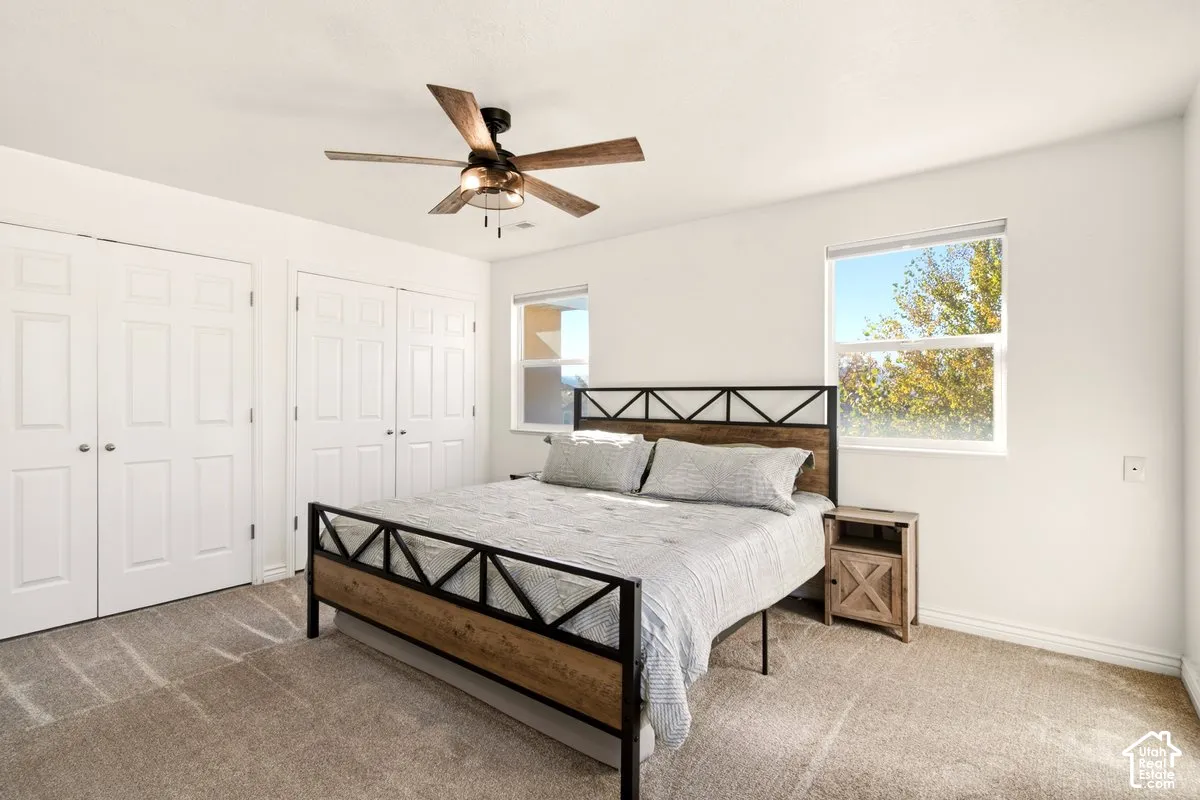 Neutral-toned carpeting, dual double-door closets, ceiling fan with integrated lighting, and dual windows