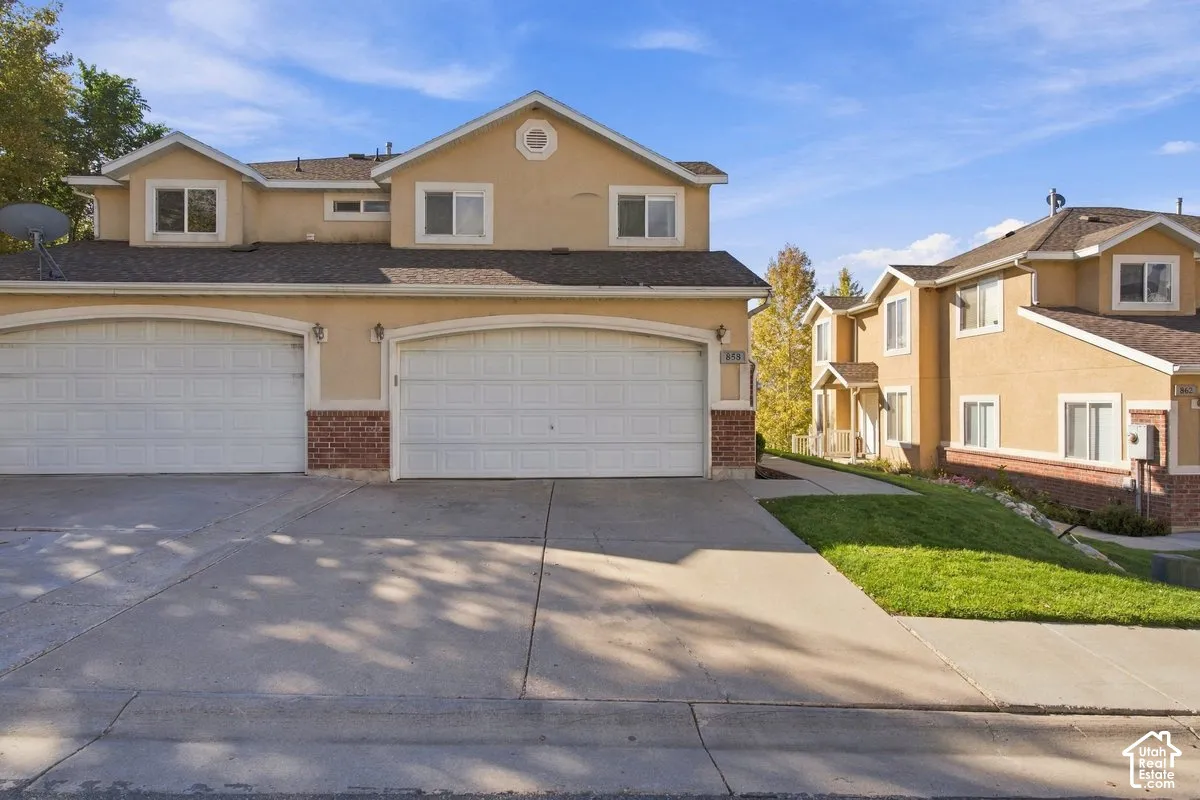 Multi-level stucco exterior with brick accents, featuring double-car garage bays, arched garage entries, and concrete driveway