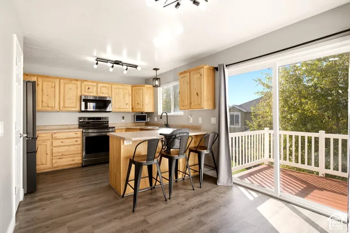 Kitchen featuring natural wood cabinetry, stainless steel appliances, a peninsula with stone-finish countertop, wood-finish flooring, and a glass sliding door opening to a deck