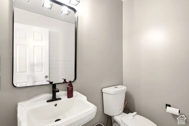 Wall-mounted rectangular mirror with a black frame, pedestal sink featuring a matte black faucet, and three-light vanity fixture