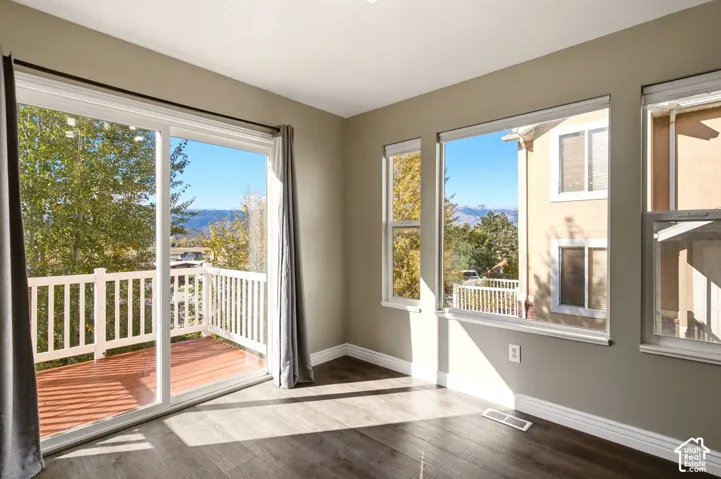 Room featuring wood-finish flooring, large windows, and a sliding glass door providing access to a deck with mountain scenery