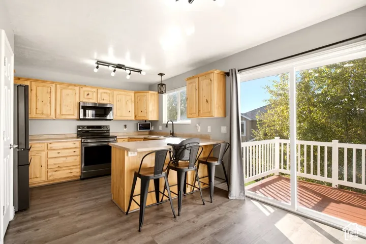 Kitchen featuring natural wood cabinetry, stainless steel appliances, a peninsula with counter seating, wood-finish flooring, and sliding glass doors opening to an elevated balcony