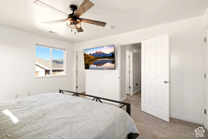 Neutral-toned bedroom featuring wall-to-wall carpeting, a ceiling fan with integrated light fixture, a dual-pane window, and a six-panel interior door