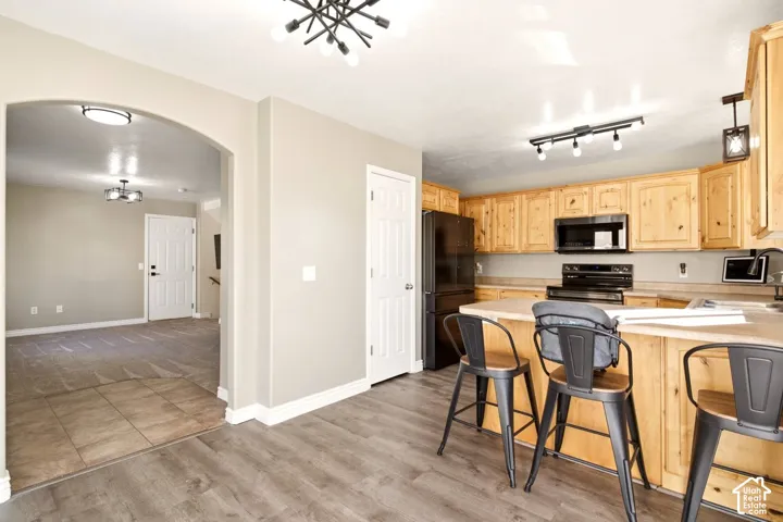 Kitchen featuring natural wood cabinetry, a center island with countertop seating, modern track lighting, and wood-finish flooring