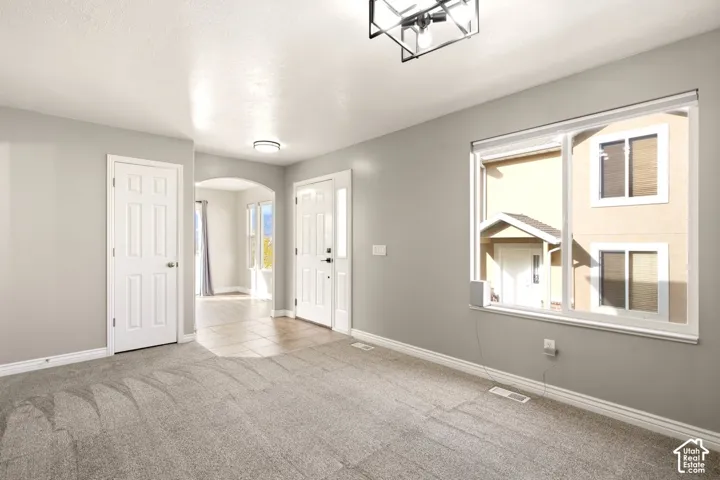 Neutral-toned interior featuring wall-to-wall carpeting, an oversized window, a geometric metal chandelier, and a decorative arched entryway