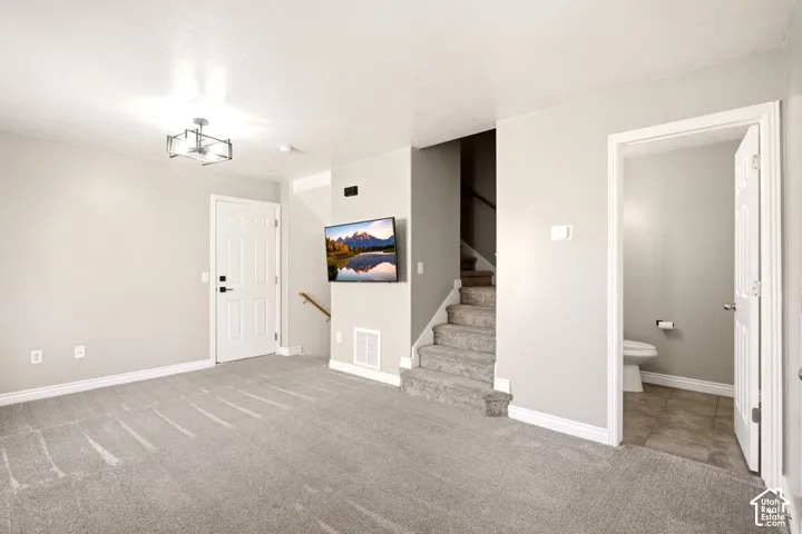 Neutral-toned interior featuring wall-to-wall carpeting, a multi-light geometric chandelier, carpeted staircase with wood handrail, and an entry door with panel detailing