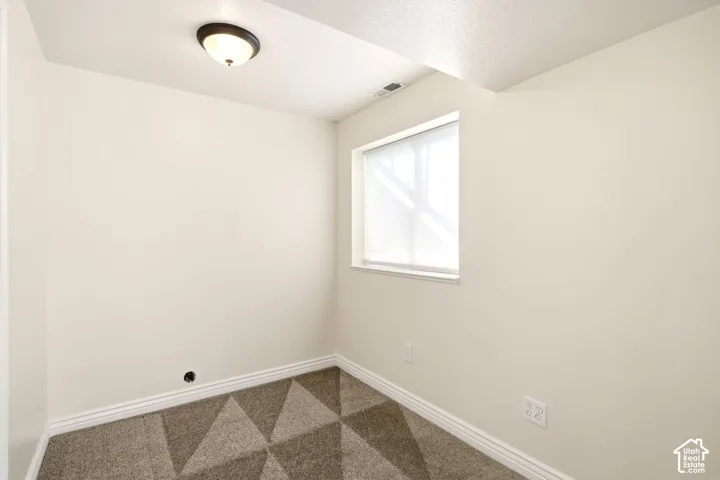 Neutral-toned interior space featuring geometric-patterned carpeting, walls with a soft-white finish, a single-pane window, and a flush-mount overhead light fixture