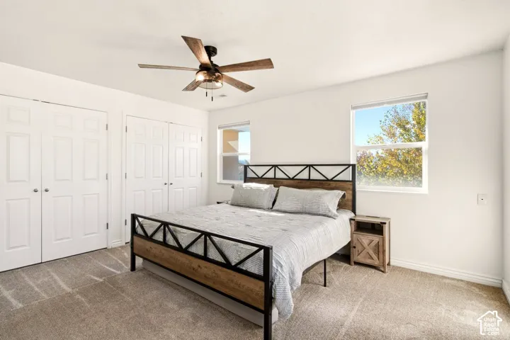Neutral-toned carpeting, dual double-door closets, ceiling fan with integrated lighting, and dual windows