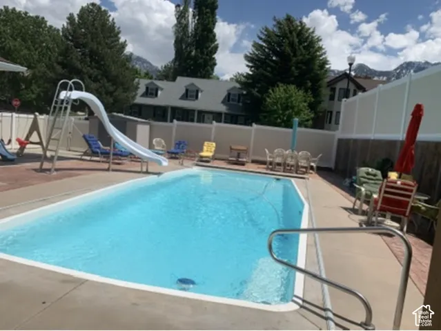 In-ground swimming pool featuring a built-in slide, concrete decking, metal safety railing, and privacy fencing with a mountainous backdrop
