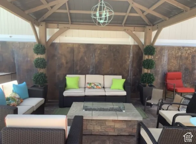 Covered outdoor gazebo featuring exposed wood beams, a metal roof, a spherical pendant light fixture, and a stone-veneer fire pit with a glass surround