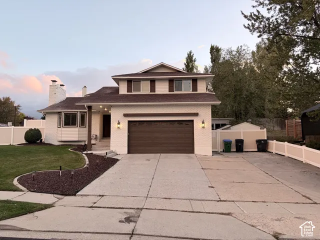 Exterior facade featuring painted brick, bay window, two-car garage, concrete driveway, and white vinyl privacy fencing