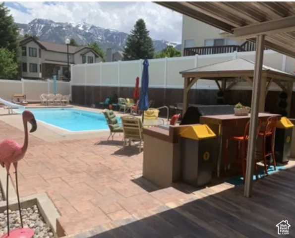 Backyard featuring an inground swimming pool with slide, stamped concrete patio, built-in outdoor kitchen with bar seating, wooden gazebo, and white vinyl perimeter fencing with a mountain backdrop