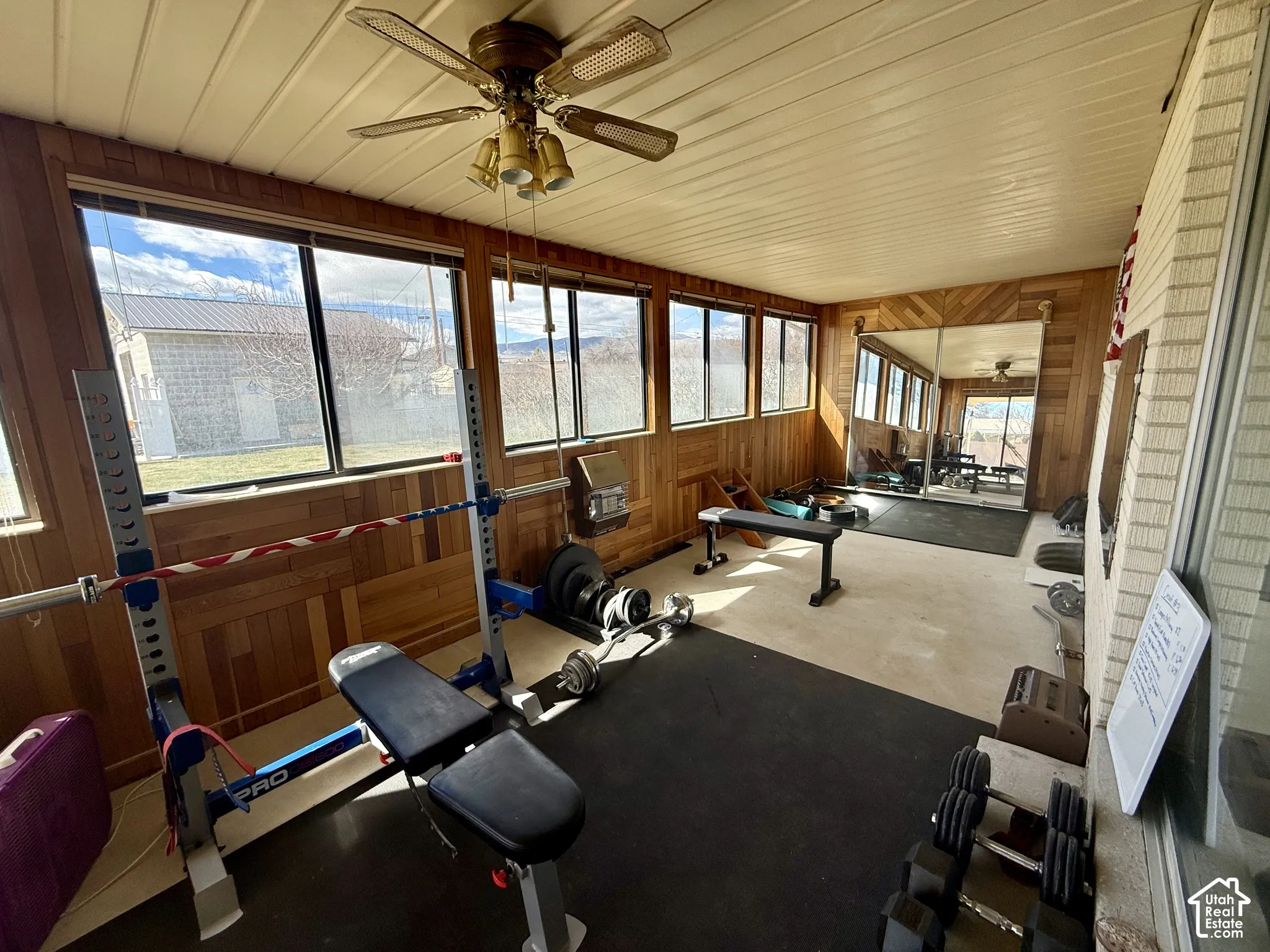 Enclosed sunroom featuring horizontal wood-paneled walls, large windows, a ceiling fan with integrated lighting, and mirror.