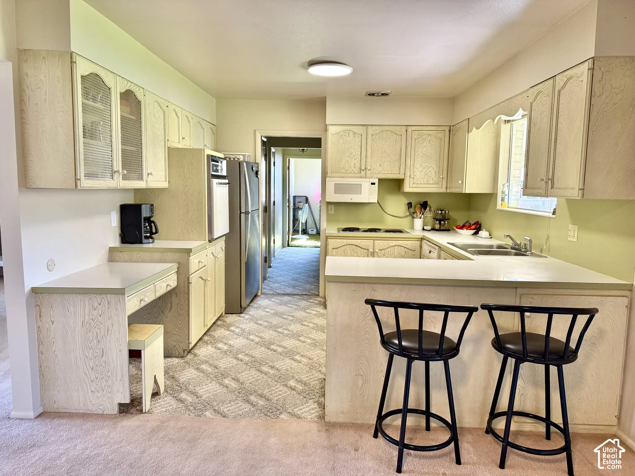 Kitchen featuring light-tone cabinetry with glass-front accents, a built-in oven, and a breakfast bar peninsula