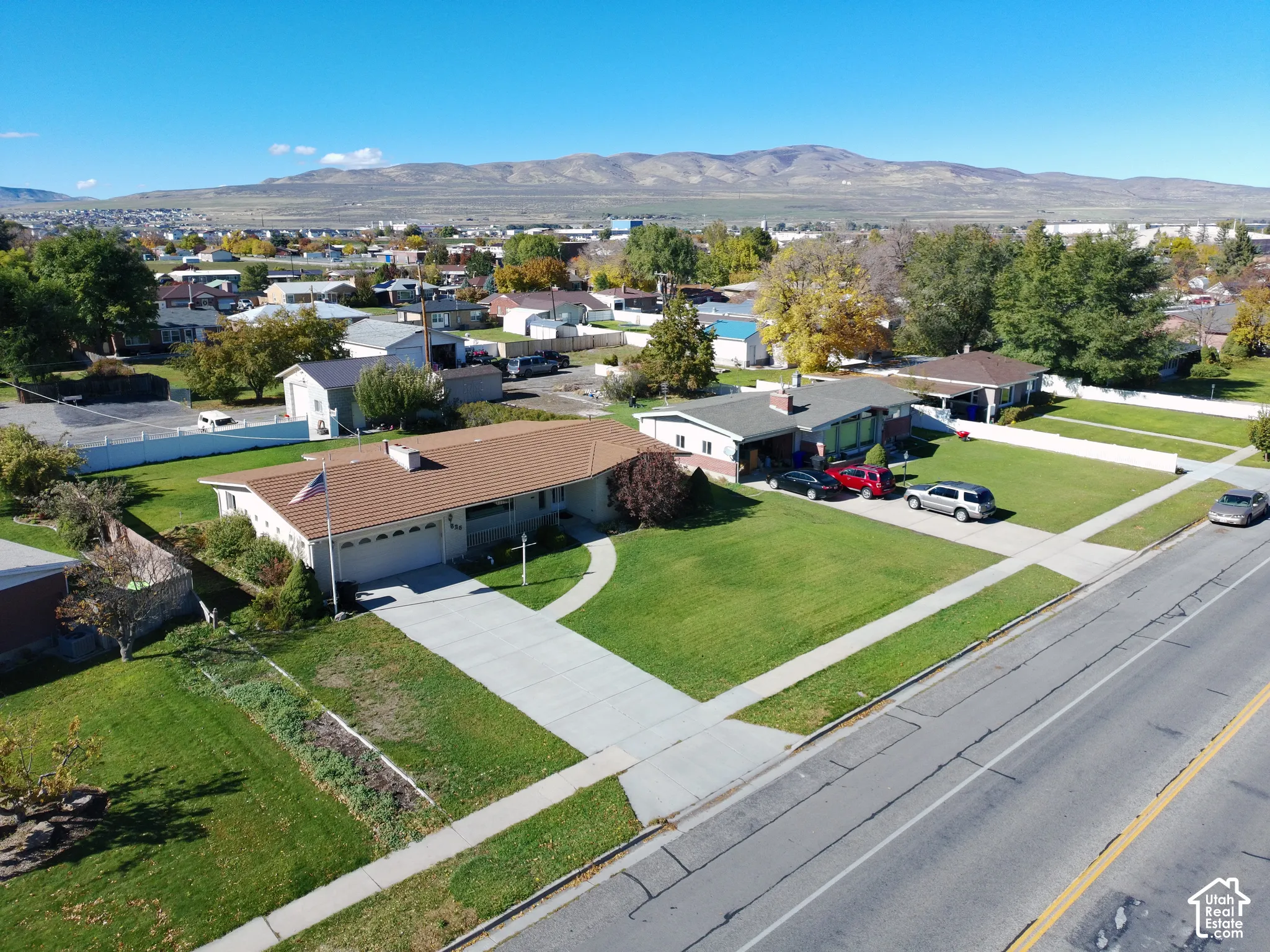 Aerial perspective featuring single-story residence featuring a concrete driveway, two-car garage, mature landscaping, and mountain backdrop