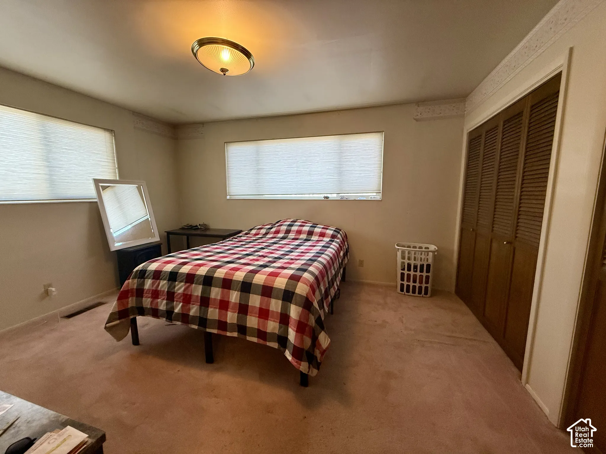 Room featuring carpeted flooring, two windows with horizontal blinds, built-in louvered-door closet, crown molding, and a central dome light fixture