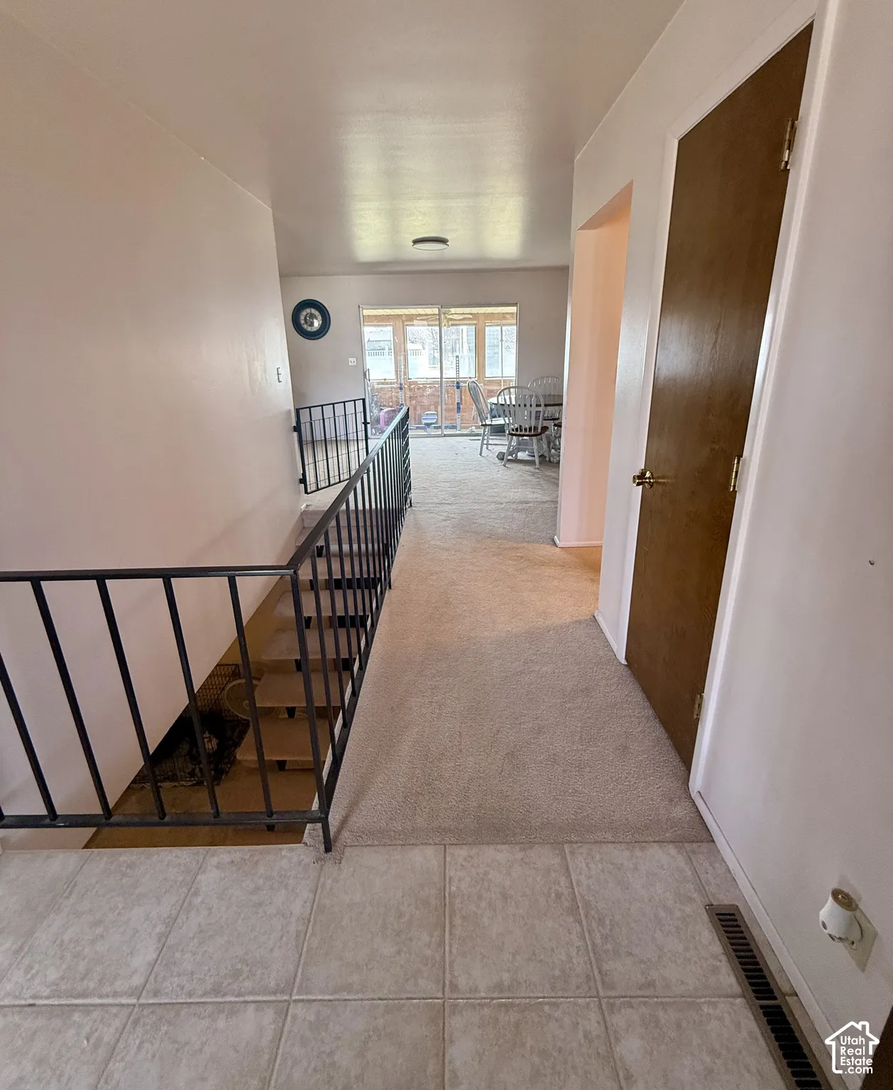 Interior hallway featuring light-toned tile flooring, carpeted surfaces, and a metal stair railing
