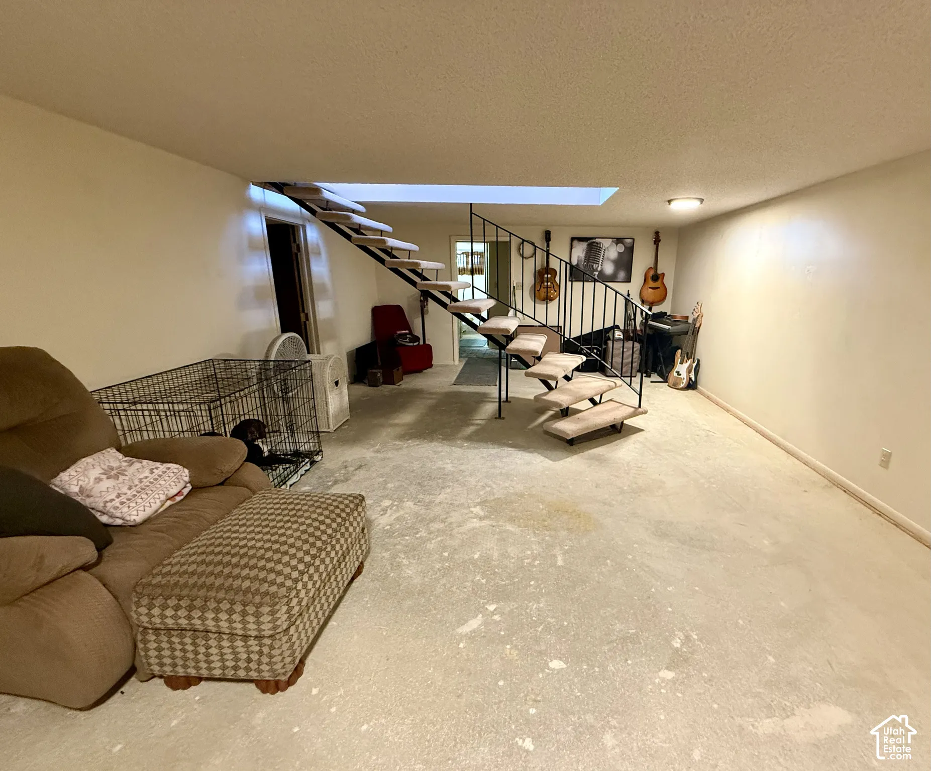 Open-concept room featuring a floating staircase with metal railings and carpeted treads, concrete flooring, and ceiling-mounted lighting