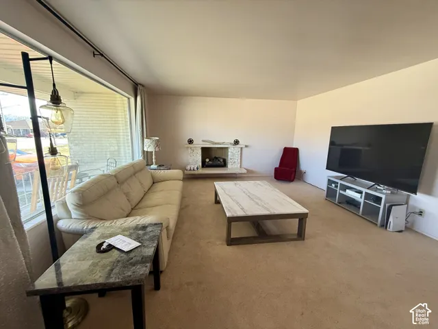 Expansive living area featuring a large picture window, wall-to-wall carpeting, and a fireplace with a textured stone facade and hearth