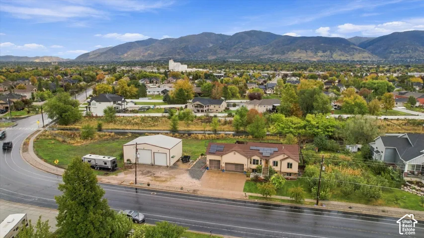 Aerial perspective of a property featuring a detached garage, solar panel array, multi-car driveway, and mountain scenery