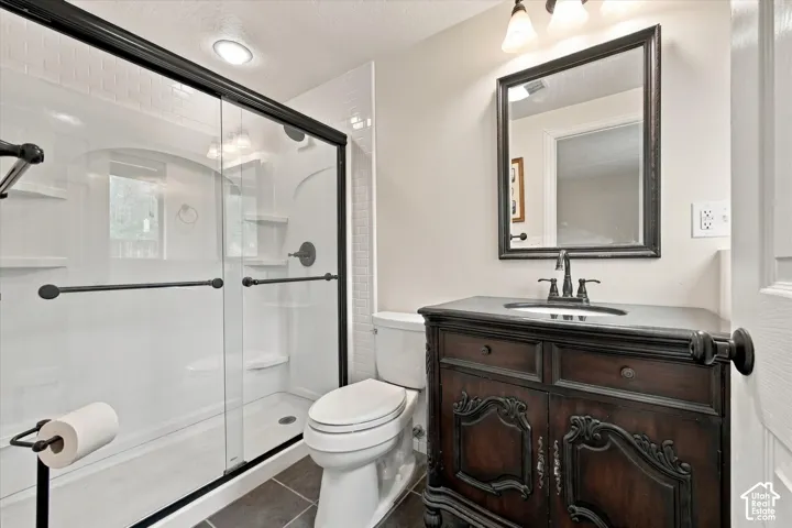 Bathroom featuring a dark wood-finish vanity with an integrated basin, shower with glass sliding doors and matte black hardware, tiled flooring, and a framed wall mirror