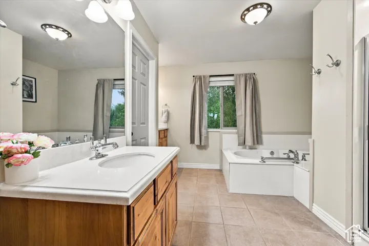 Bathroom featuring a vanity with a white countertop and undermount sink, ceramic tile flooring, deep soaking tub with chrome fixtures, and a large wall-mounted mirror