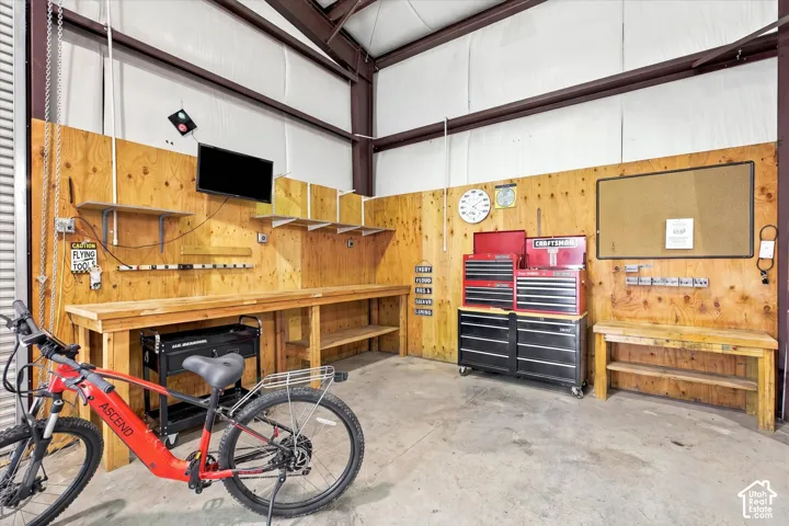 Workshop area featuring wood-paneled walls, expansive custom-built wood workbenches, open shelving, exposed metal structural beams, and concrete flooring