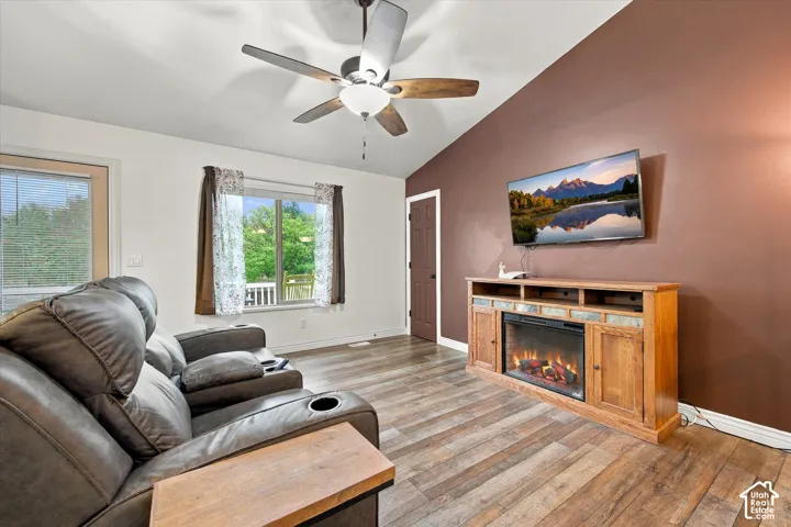 Vaulted ceilings, wood-finish flooring, accent wall, and a multi-blade ceiling fan