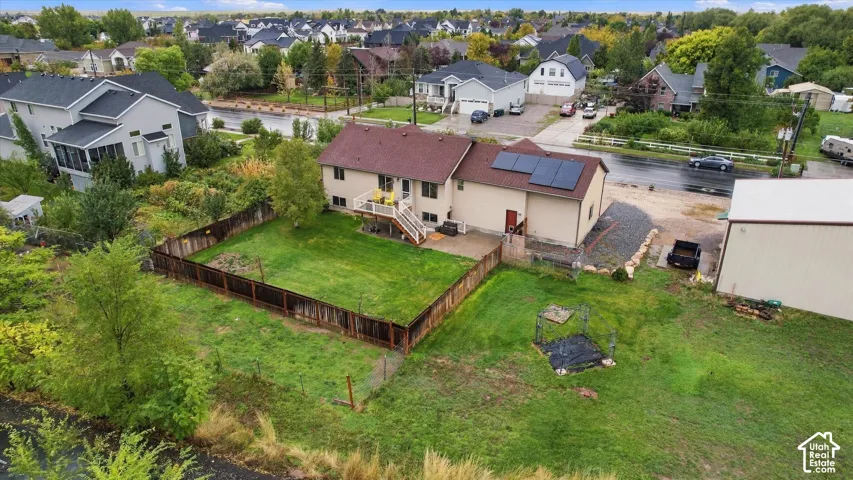 Aerial perspective of property featuring an elevated deck, roof-mounted solar panels, wood-slat fencing enclosing a portion of the lawn, and a detached outbuilding