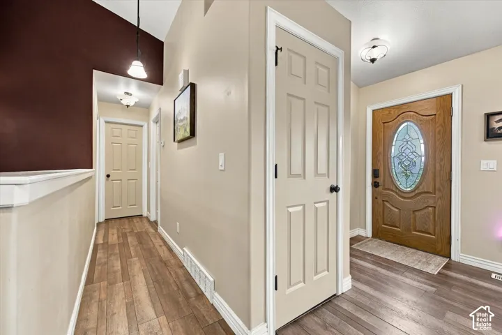 Entryway featuring wood-finish flooring, a solid wood front door with an oval glass insert, vaulted ceilings, and dual flush-mount ceiling light fixtures