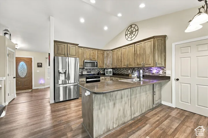 Kitchen featuring vaulted ceilings, recessed lighting, wood-finish cabinetry, a central island with a solid surface countertop, and stainless steel appliances