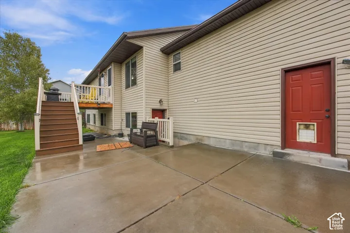 Exterior featuring light-toned horizontal siding, concrete patio, elevated wooden deck, and stairway with metal railing