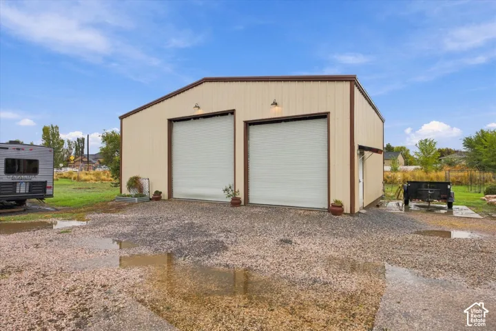 Detached metal building featuring a dual-bay configuration, roll-up garage doors, wall-mounted exterior lighting, and a gravel driveway