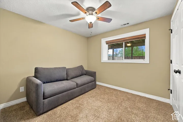Neutral wall coloring, carpeting, horizontal sliding window with white trim, and a five-blade ceiling fan with an integrated light fixture
