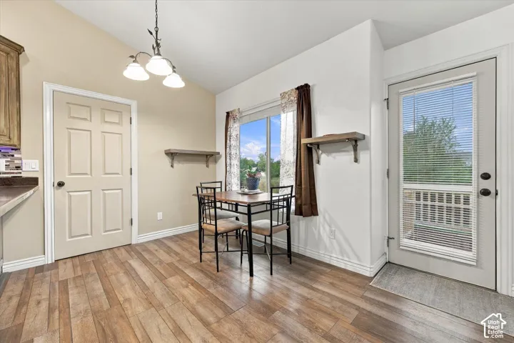 Vaulted ceiling featuring a three-light pendant fixture, wood-finish flooring, and a glass-paneled exterior door