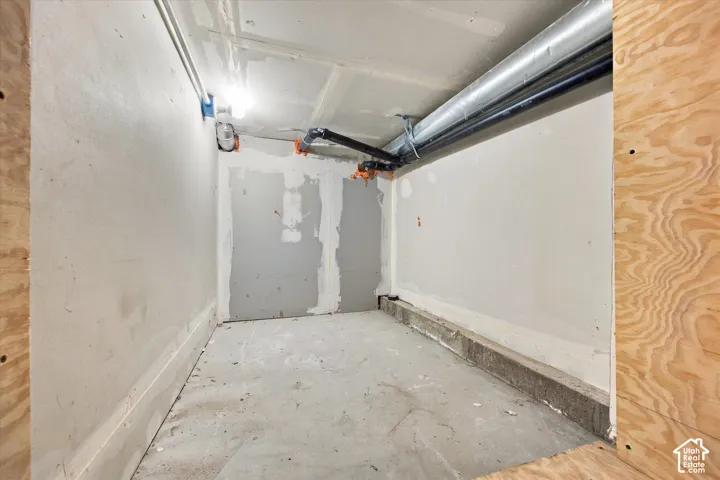 Enclosed utility room featuring unfinished drywall, concrete flooring, and exposed piping
