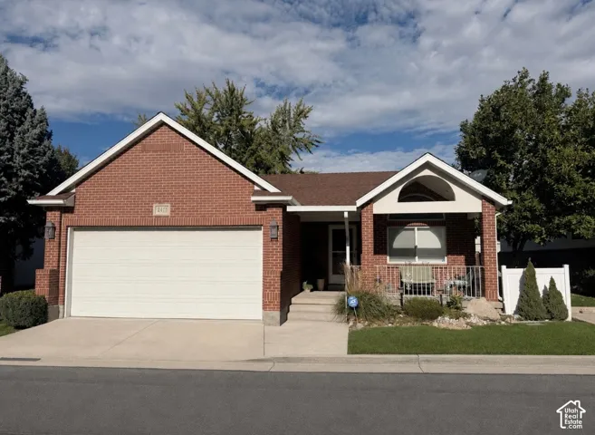 Red brick exterior featuring a covered front porch, gabled roofline, concrete driveway, and attached two-car garage