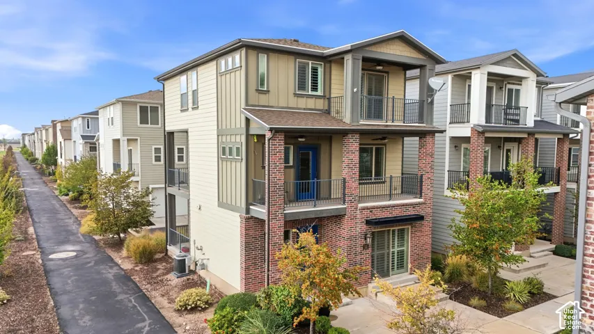 Multi-level exterior featuring a brick and composite siding facade, two private balconies with metal railings, and a concrete patio