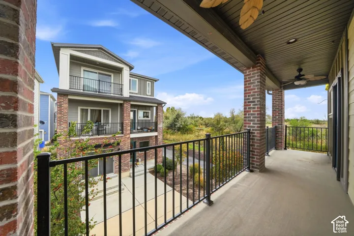Covered balcony featuring concrete flooring, ceiling fan, and black metal railings with brick column supports