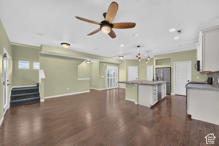 Open-concept interior featuring wood-finish flooring, a central kitchen island with stone-finish countertops, multi-bulb pendant lighting, a ceiling fan with integrated illumination, and recessed lighting