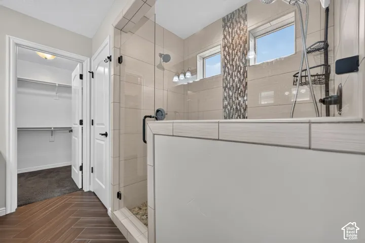 Primary Bath with walk-in shower featuring a frameless glass door, horizontal wall tile, vertical mosaic tile accent, pebble-style shower floor, and herringbone wood-finish flooring
