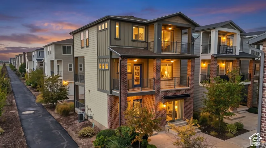 Multi-story residence featuring brick and vertical siding exterior, dual stacked covered balconies with metal railings, and concrete patio hardscaping