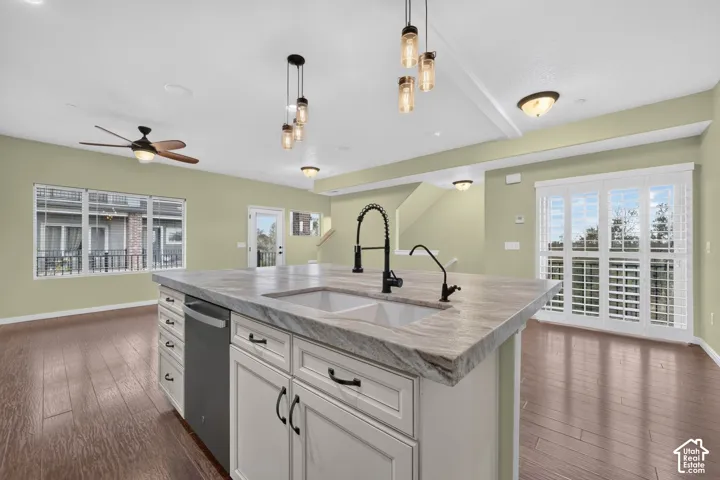 Kitchen island with stone-finish countertop, dual basin undermount sink, matte black gooseneck faucet, white cabinetry, and wood-finish flooring